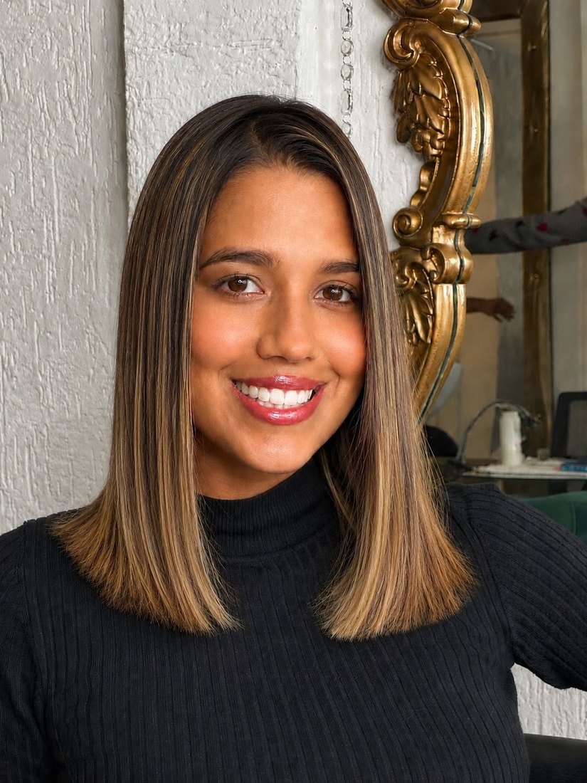 Clienta sonriendo con una media melena lisa en tonos bronde y mechas que enmarcan el rostro.