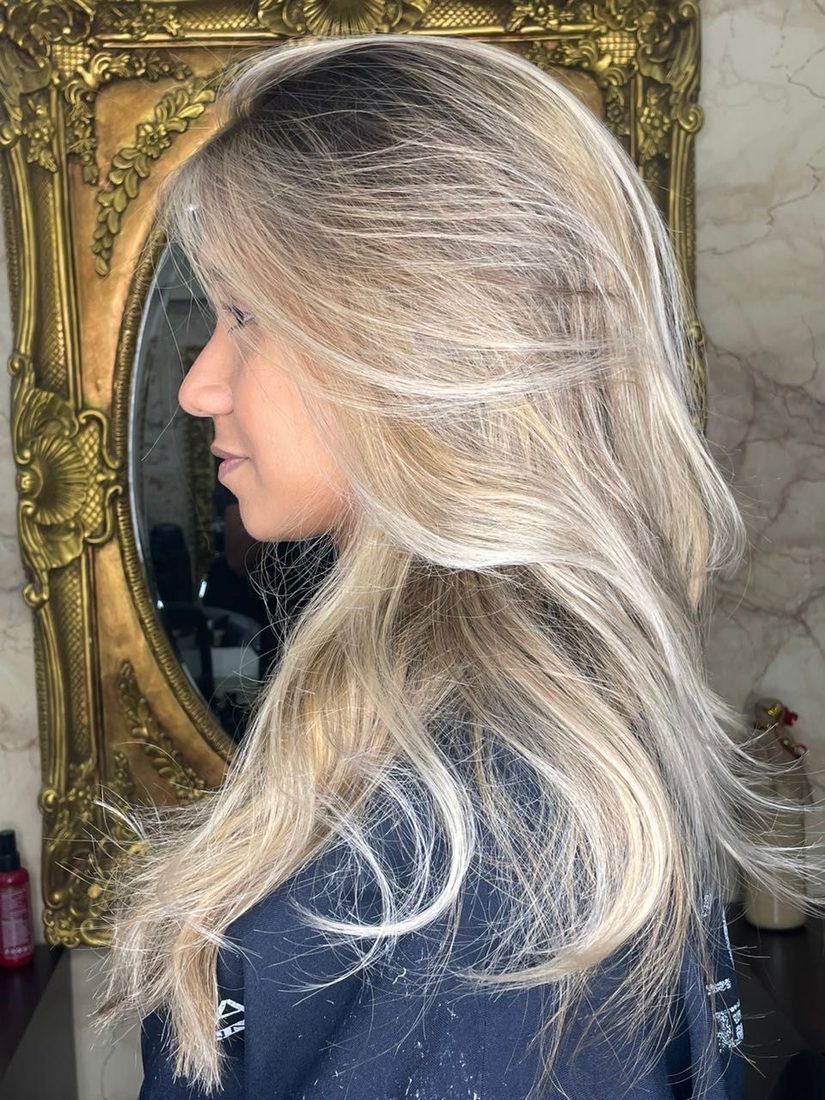 Clienta de perfil ante un espejo dorado, con melena larga en capas en rubio platino.